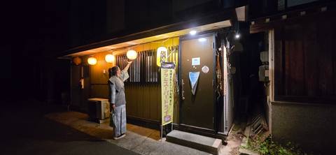       Man in yukata reaches for a lantern-lit entrance of a small izakaya at night
  