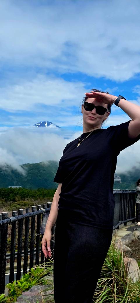       Close-cropped portrait of woman in sunglasses with distant Mount Fuji above clouds
  
