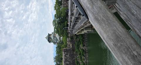       Osaka Castle rising behind a stone bridge over a green moat under mottled clouds
  