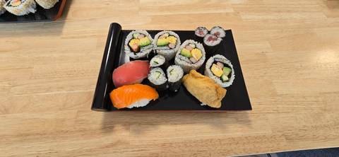       Assorted sushi rolls, nigiri and inari neatly arranged on a lacquer tray on wooden table
  