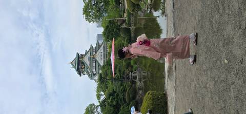       Woman in pink kimono with parasol passes reflective pond with Osaka Castle behind
  