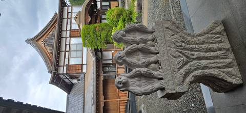       Stone sculpture of the three wise monkeys displayed on a pedestal outside a wooden building
  