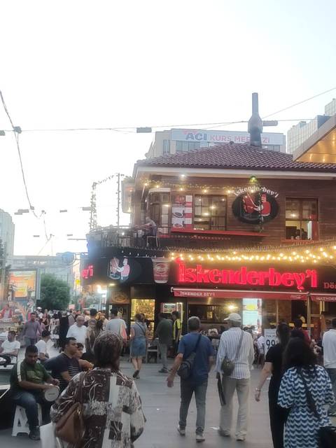       Busy street corner restaurant sign illuminated by string lights at dusk
  