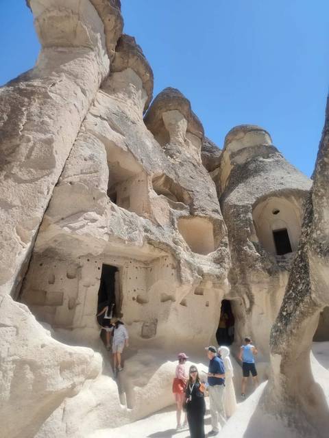       Ancient rock-cut dwellings and conical formations under bright blue sky
  