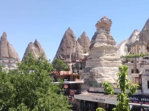       Cluster of fairy-chimney rock spires beside village buildings and trees
  