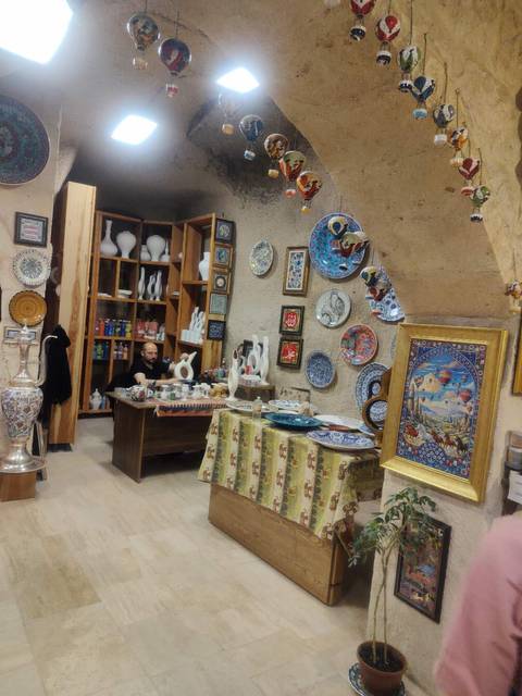       Artisan seated among handmade ceramic plates and pottery inside workshop
  
