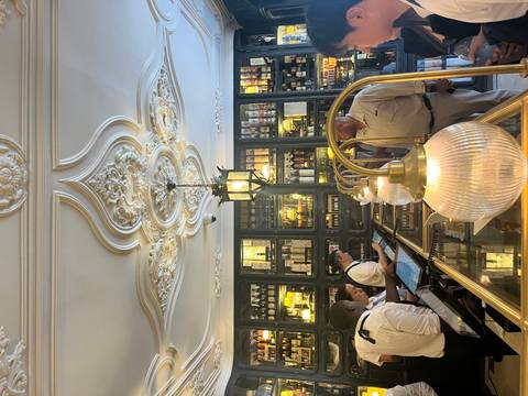       Elegant historic patisserie interior with ornate ceiling and staff serving at a glass counter
  