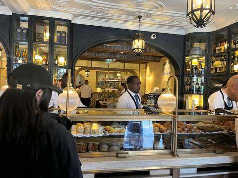       Busy bakery counter filled with pastries and golden décor, staff serving behind glass
  