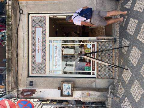       Storefront of Fábrica da Nata pastelaria with decorative tile border and sidewalk sign
  
