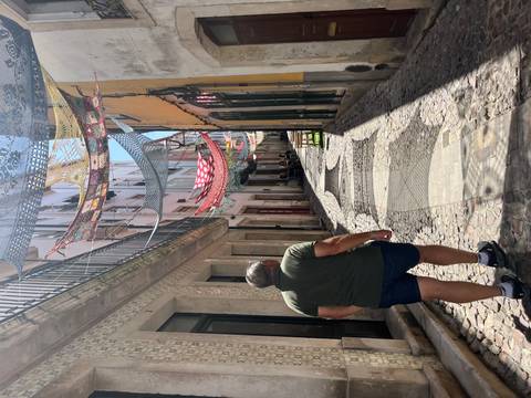       Narrow sunlit alley with colorful fabric canopies overhead and cobbled pathway
  