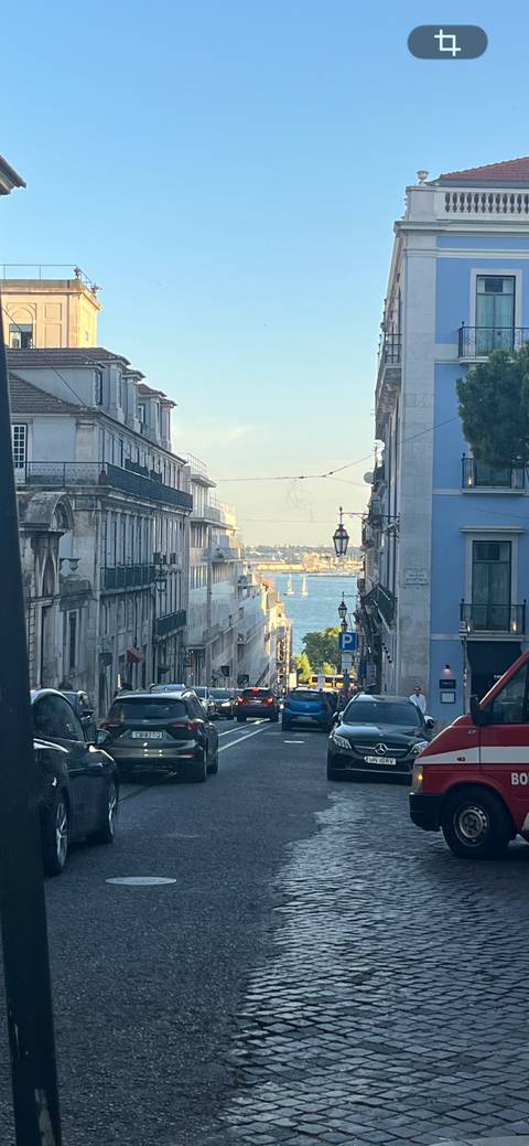       Urban street canyon descending toward the Tagus with sailboats visible beyond
  
