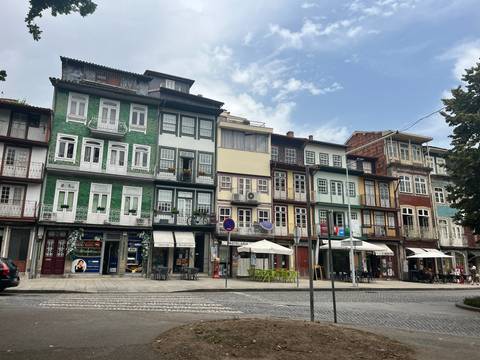       Row of colorful narrow townhouses with cafés in front of a cobblestone square
  