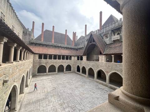       Stone courtyard of a medieval palace with arched cloisters and red tiled roofs
  