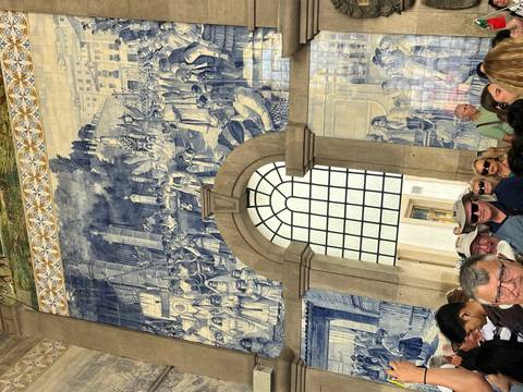       Crowded hall of São Bento Station displaying vast blue azulejo mural scenes
  