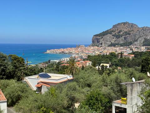       Blue Mediterranean bay with the historic town of Cefalù stretching along the shore beneath a rocky promontory
  