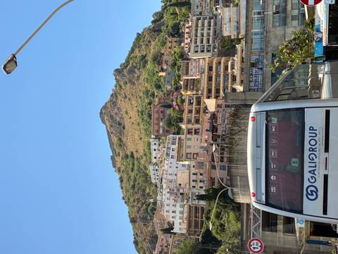       City hillside with layered apartment blocks and a tourist coach in the foreground beneath a clear sky
  