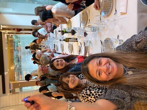       Long restaurant table filled with smiling tour members enjoying wine and conversation indoors.
  