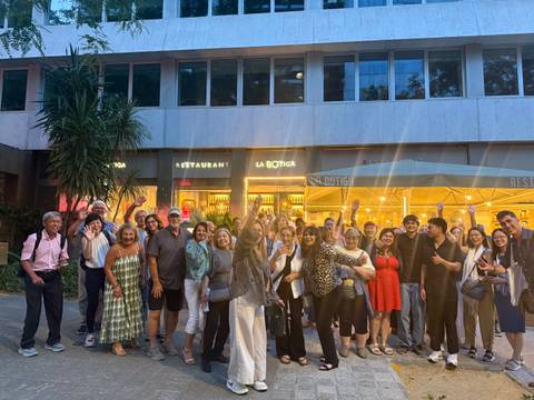       Large tour group gathered outside a city restaurant in dusk light, many waving at the camera.
  