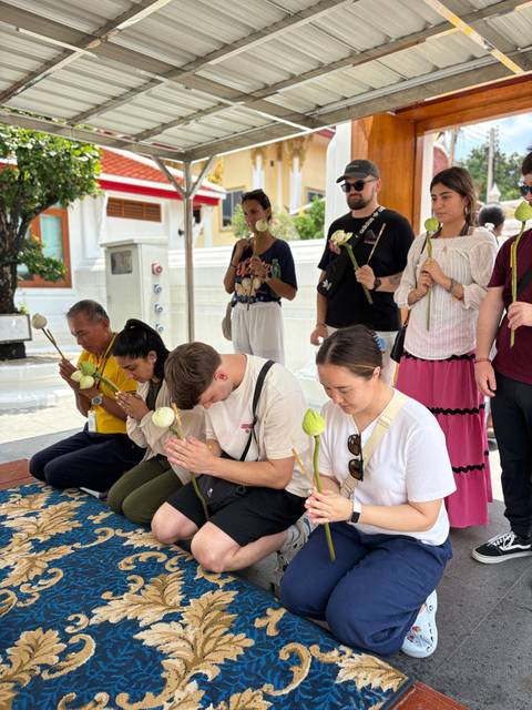       Travellers kneel with lotus buds during a traditional prayer ritual inside a Thai temple.
  
