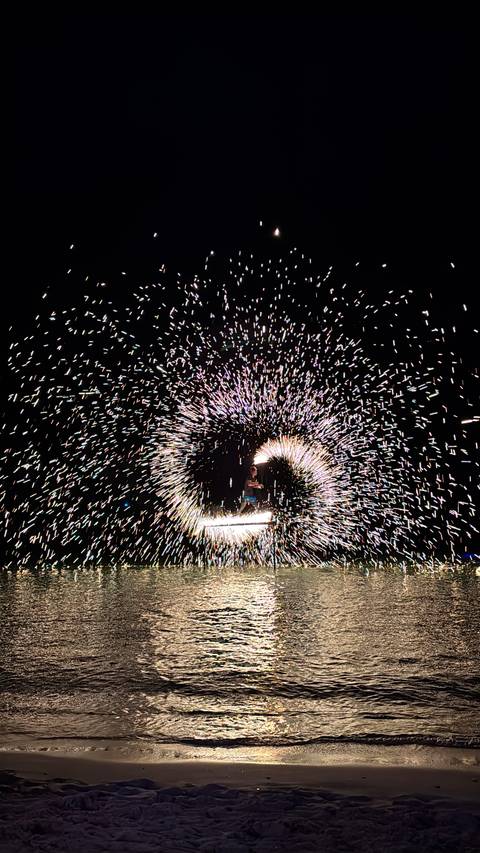       A performer spins flaming steel wool, creating a dazzling spiral of sparks in the night.
  