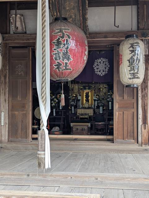       Interior of a Japanese shrine with large red paper lanterns framing an ornate altar of drums and statues.
  