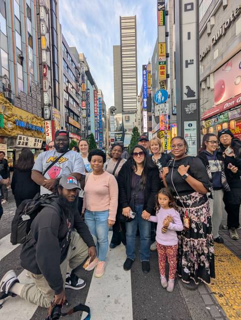       Tour group poses on a busy neon-lit street in Shinjuku with colorful signs towering behind.
  