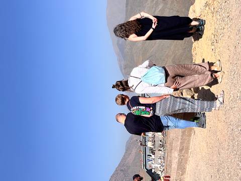       Tourists stand at a mountain lookout, gazing over arid valleys beneath a cloudless sky.
  