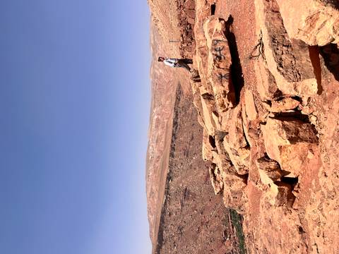       Lone traveler stands on red sandstone outcrop overlooking a vast arid plateau and blue sky.
  