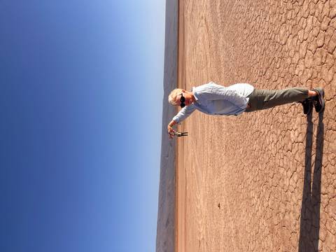       Woman poses with outstretched arm creating a forced-perspective illusion on a cracked desert lakebed.
  
