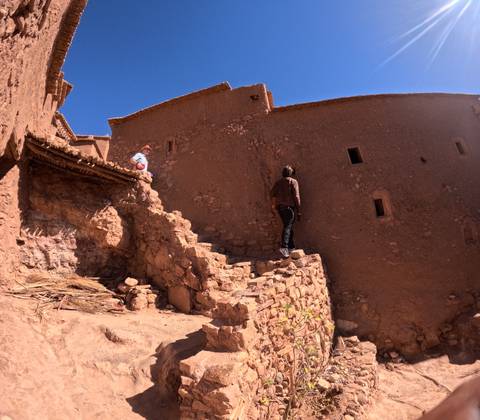       Travelers climb stone steps of an earthen kasbah, studying its ancient walls.
  