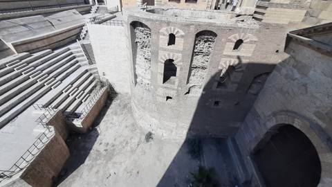       Aerial view down into ancient stone amphitheater walls and stepped seating partly in shadow.
  