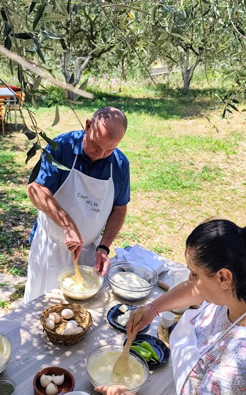       An instructor stirs dough outdoors during a countryside cooking class while a participant watches.
  