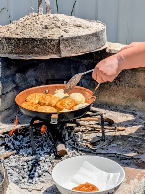       Golden dough pieces fry in a copper pan over an open wood fire during a traditional cooking session.
  