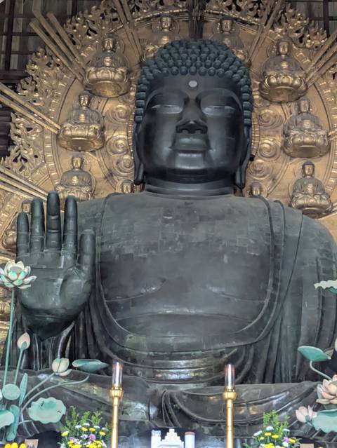       The massive bronze Buddha statue raises a hand in blessing against an ornate golden backdrop.
  