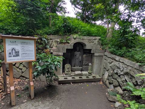       Stone Buddhist reliefs are set into a shaded hillside niche surrounded by dense foliage.
  