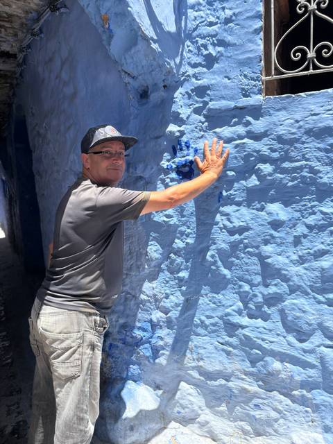       Man leaves a blue handprint on textured blue wall in narrow Chefchaouen street
  