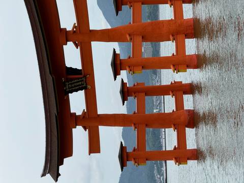      Iconic vermilion torii gate rises from the sea with mountains faintly visible behind.
  