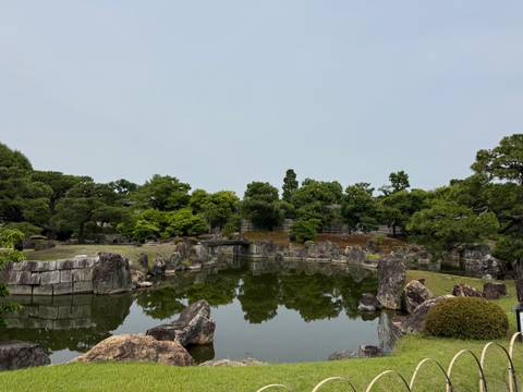       Serene Japanese garden pond reflecting scattered rocks and manicured greenery under a pale sky.
  