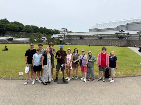       Tour group poses on the lawn in front of a traditional Japanese castle wall.
  
