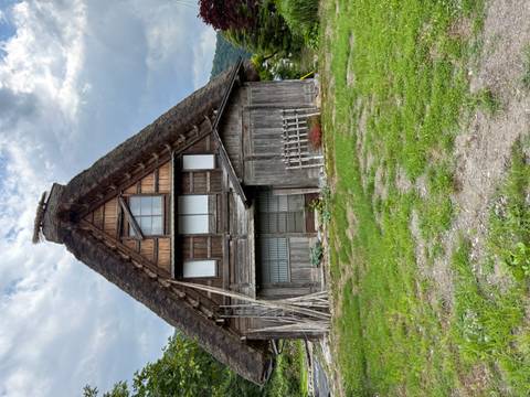       Traditional steep-roofed wooden farmhouse set against a cloudy sky and lush hillside.
  