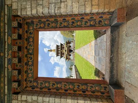       Bhutanese temple framed by a richly painted doorway across a manicured lawn under blue sky
  