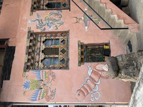       Traditional Bhutanese house facade painted pink with ornate window frames and dragon murals
  