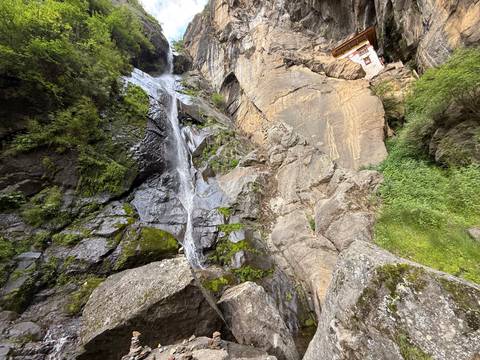       Steep rocky cliff with thin waterfall cascading beside bright green moss
  