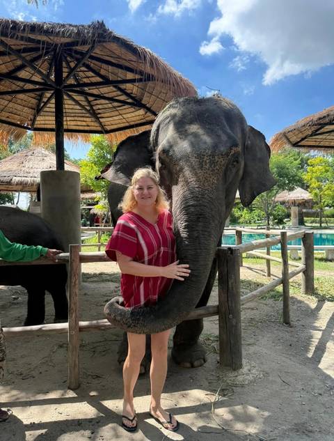       Woman in red striped shirt standing with a friendly elephant at a sanctuary poolside.
  
