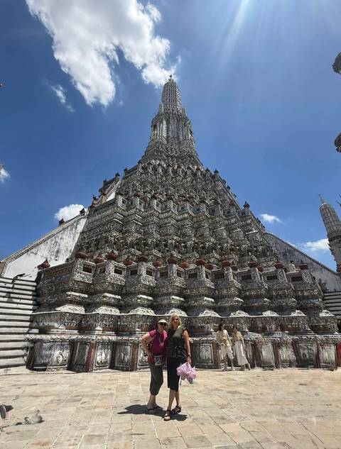       Upward view of the ornate spire and intricate façade of Wat Arun against a clear blue sky.
  