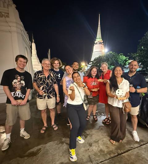       Nighttime street food tour group smiling and holding treats with a brightly lit stupa in background.
  