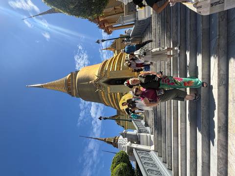       Two travelers stand on marble steps leading up to a gleaming golden chedi in bright midday sun.
  