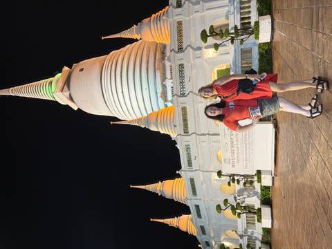       Nighttime portrait of two women standing before an illuminated white pagoda with green accent lighting.
  