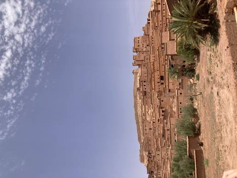       Clay-built kasbah village rises on a hilltop under a speckled sky in southern Morocco.
  