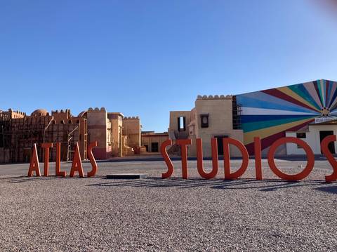       Bright red 3-D letters spell ATLAS STUDIOS at a desert film backlot under clear blue sky.
  